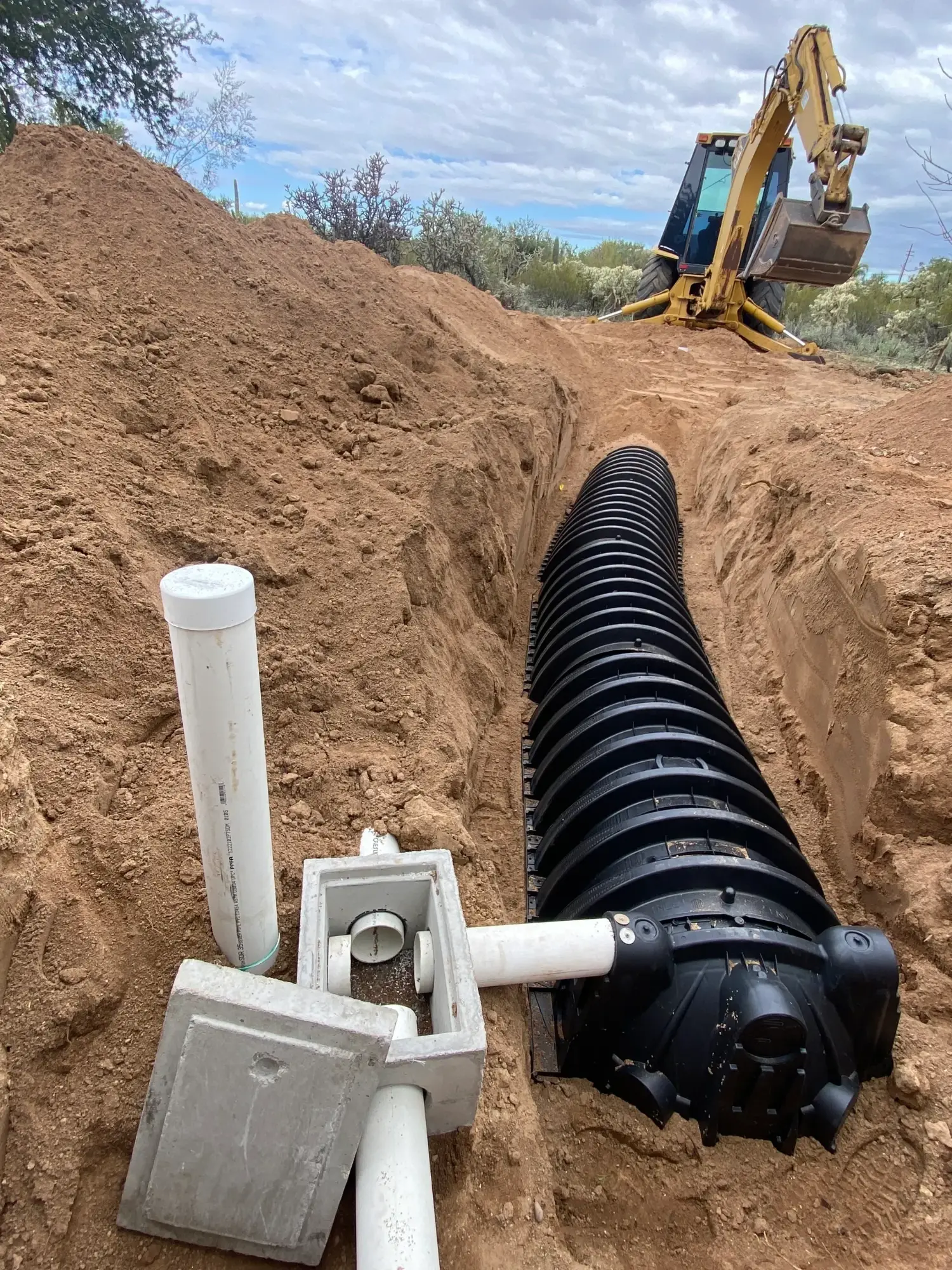Excavator laying new drain field piping in a trench